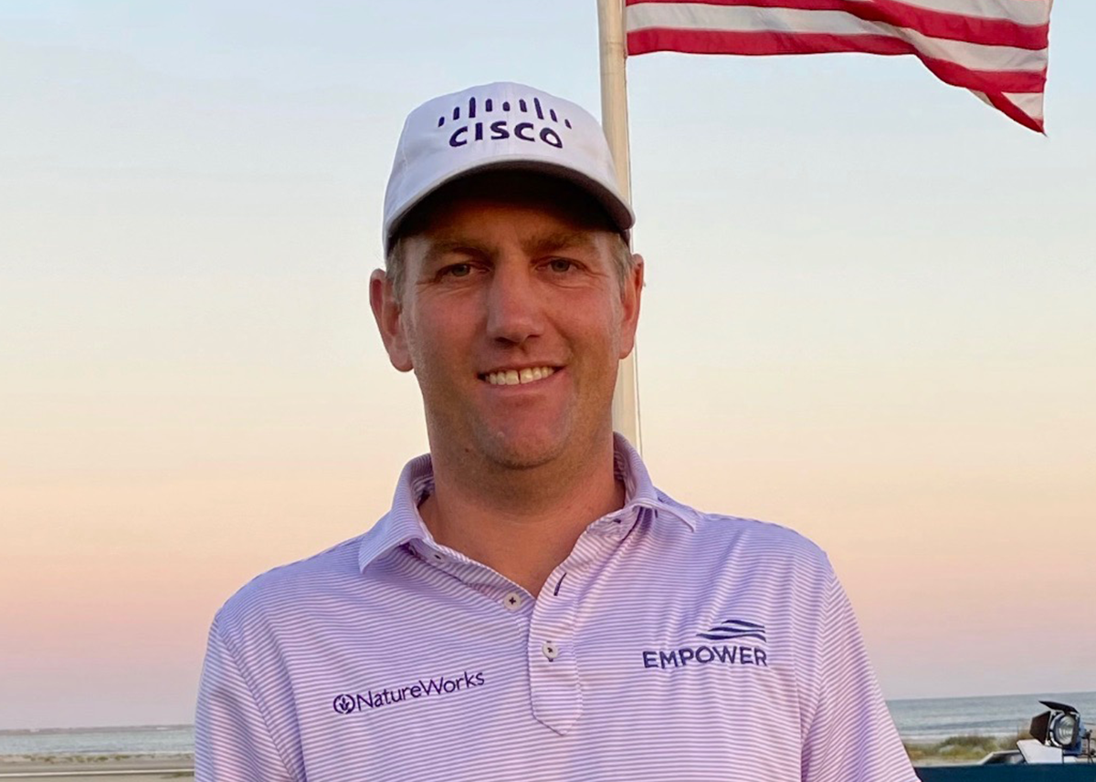 a man wearing a hat and standing in front of a flag